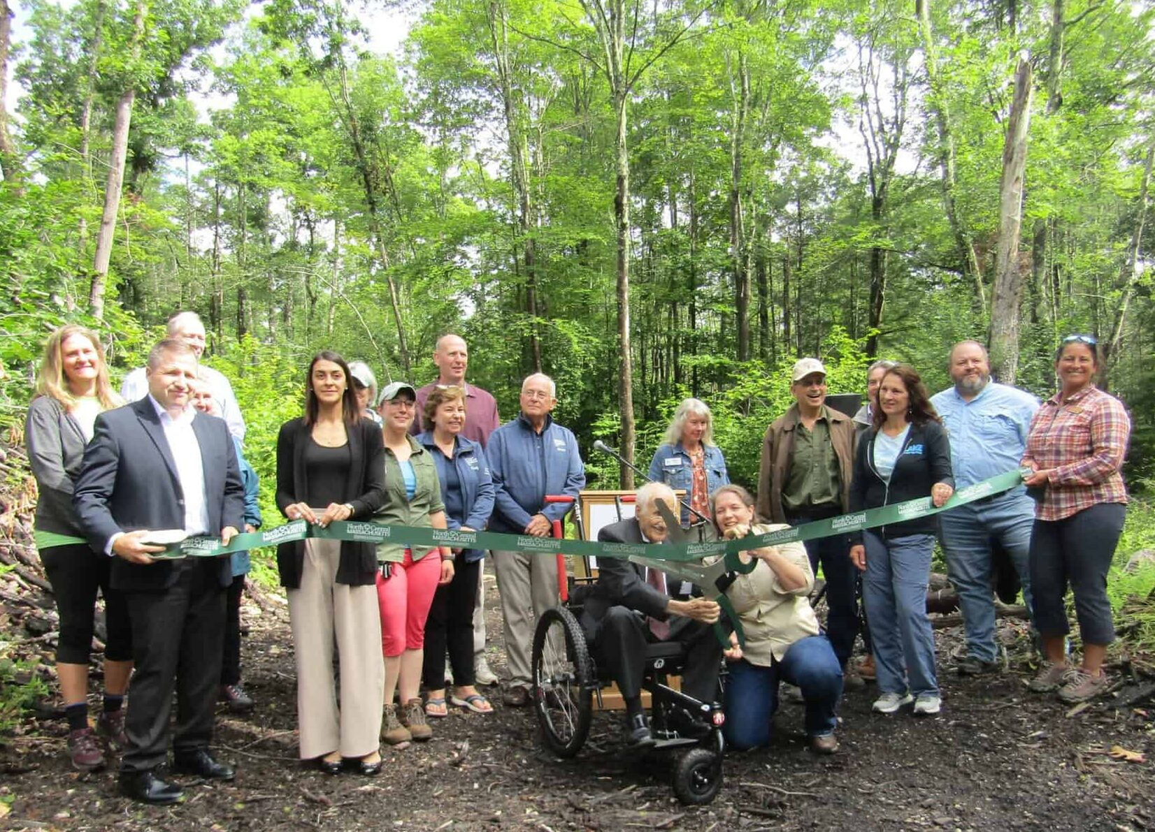 A group gathers to cut a ribbon in celebration of the official opening of the Monomonac Hill Conservation Area in Winchendon.