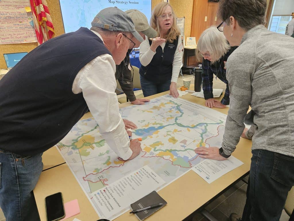A group of people surround a map discussing ideas and sharing information.